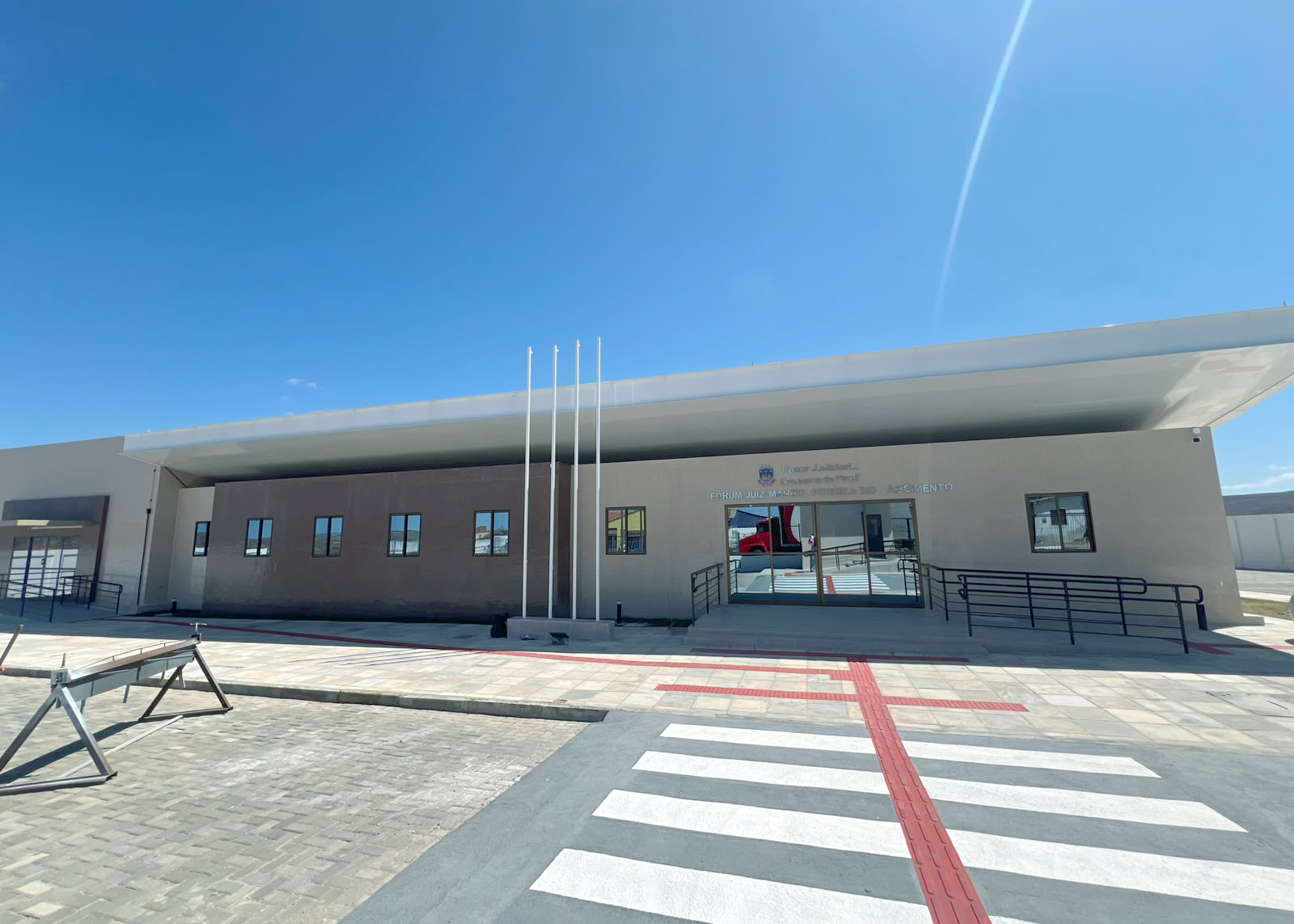 Prédio retangular, na cor bege, com parede em tijolos vermelhor e coberta reta 